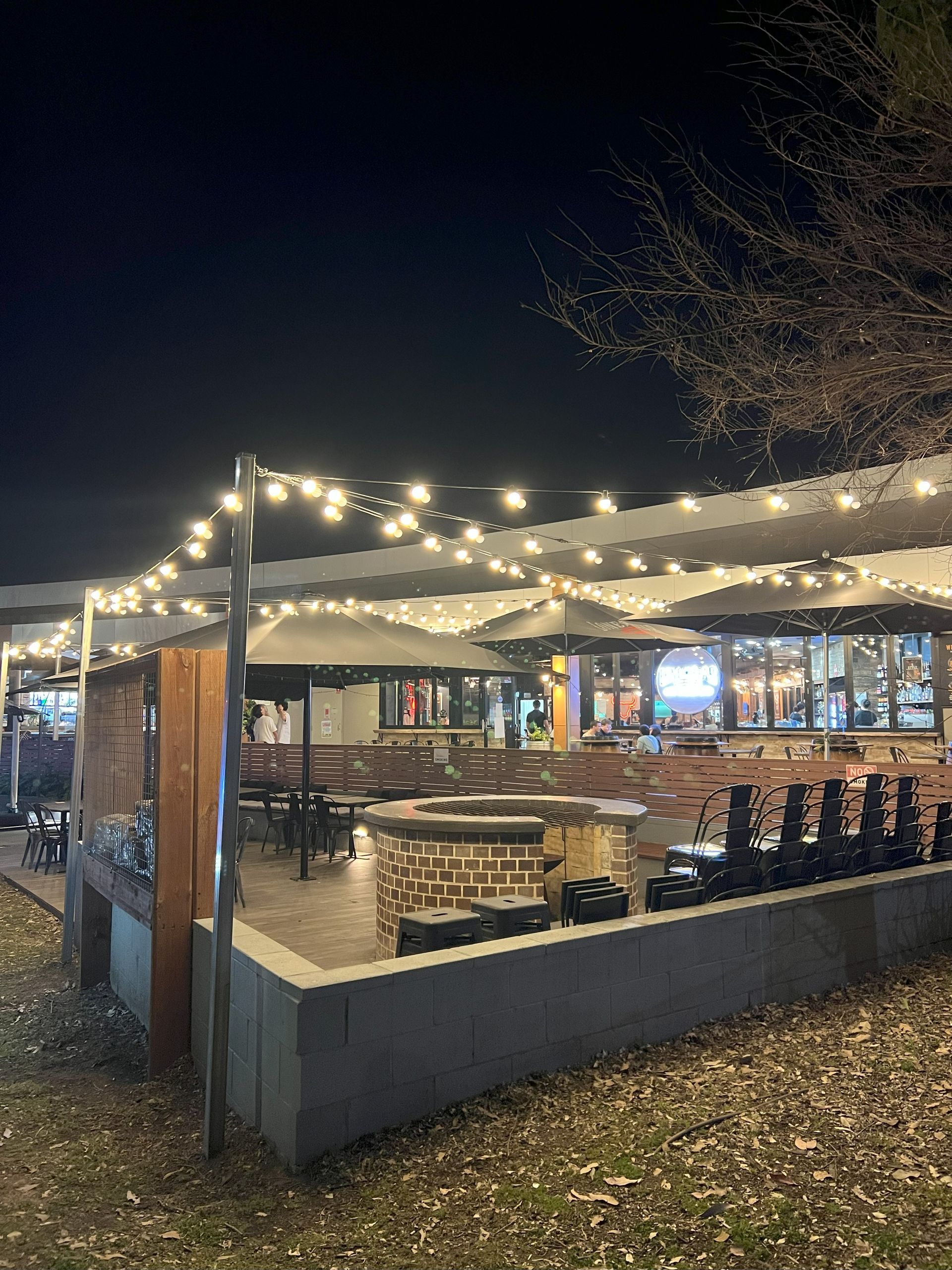 An outdoor patio at night with string lights, tables, and a bar.
