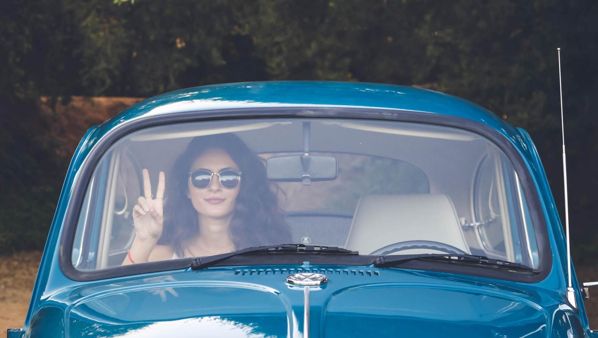 a woman is sitting in a blue car giving a peace sign .