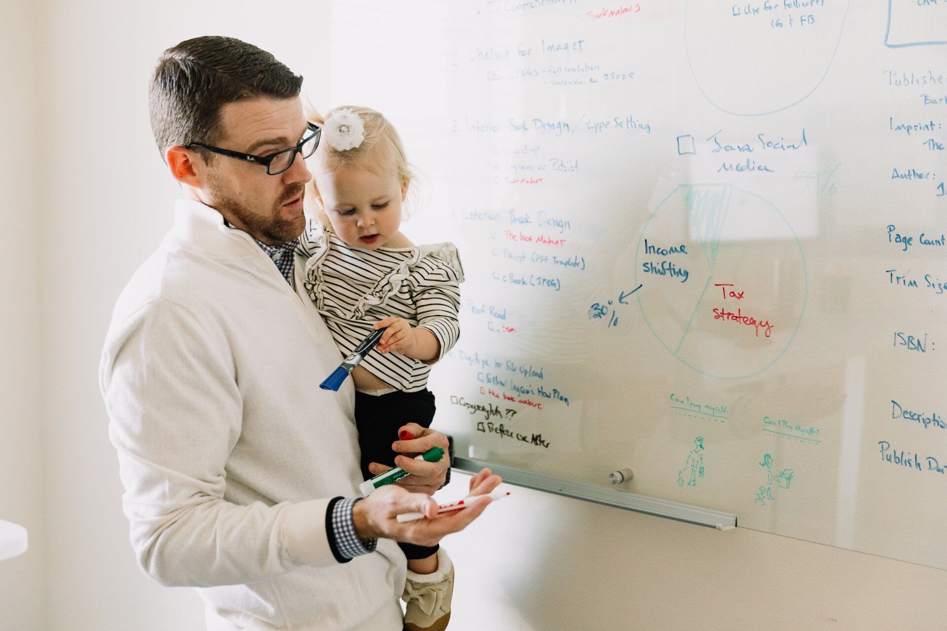 A man is holding a little girl in front of a whiteboard.