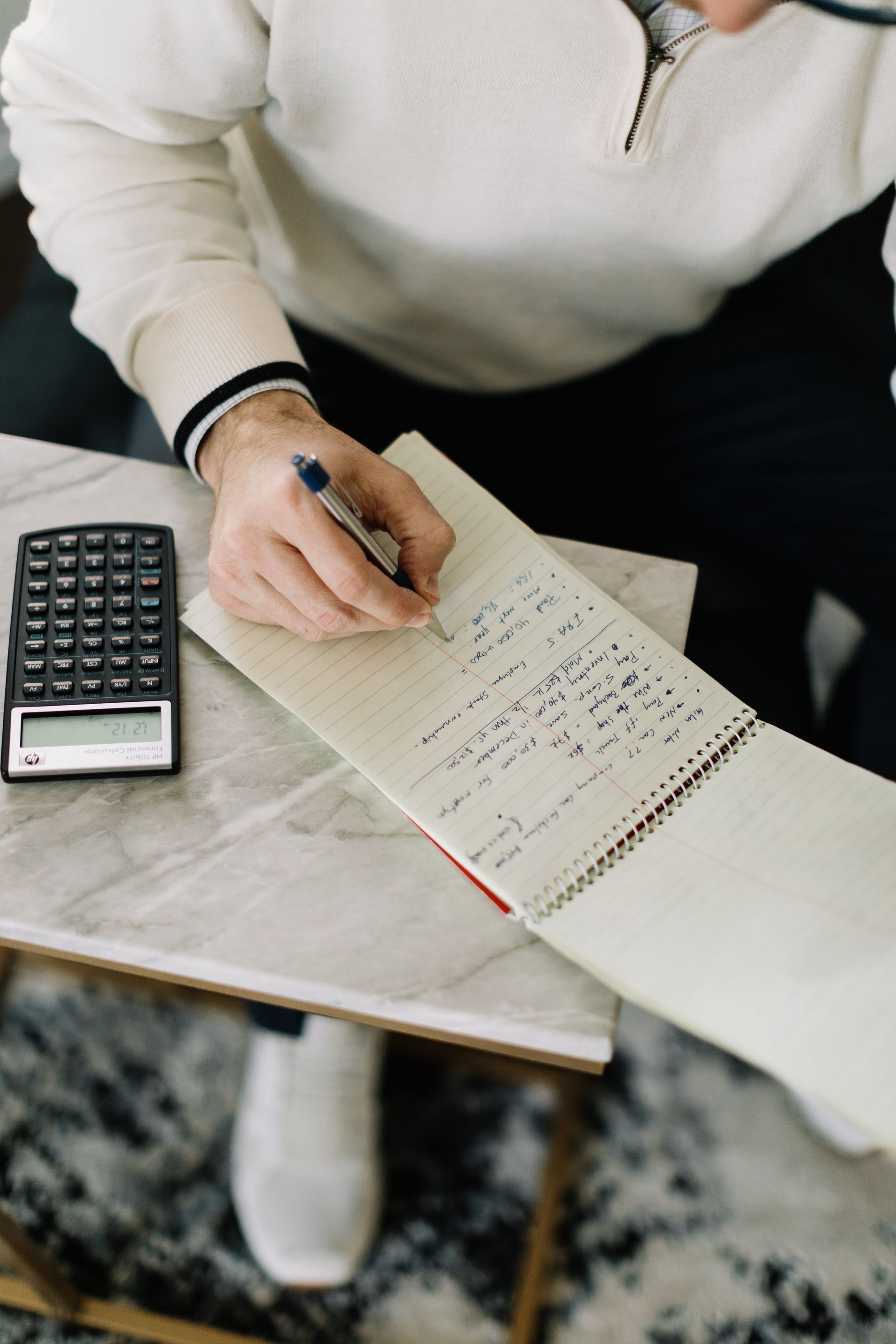 A person is writing in a notebook next to a calculator.