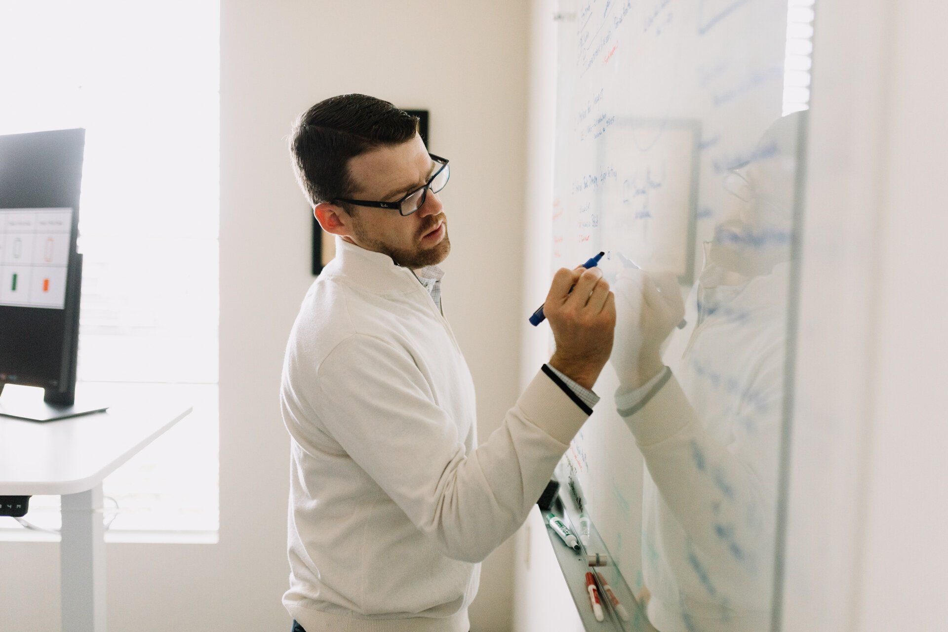A man is writing on a whiteboard with a marker.