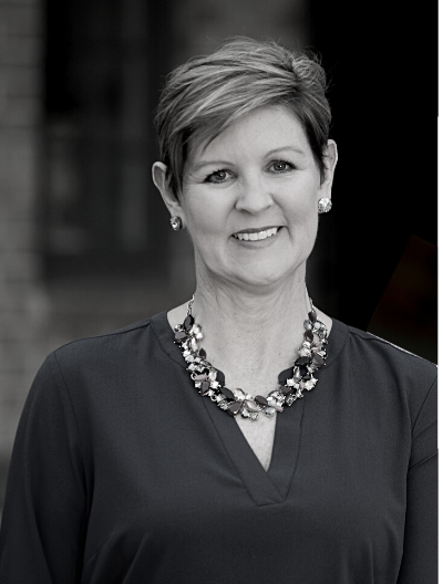 Leah Stradley photo A woman wearing a necklace and earrings is smiling in a black and white photo.