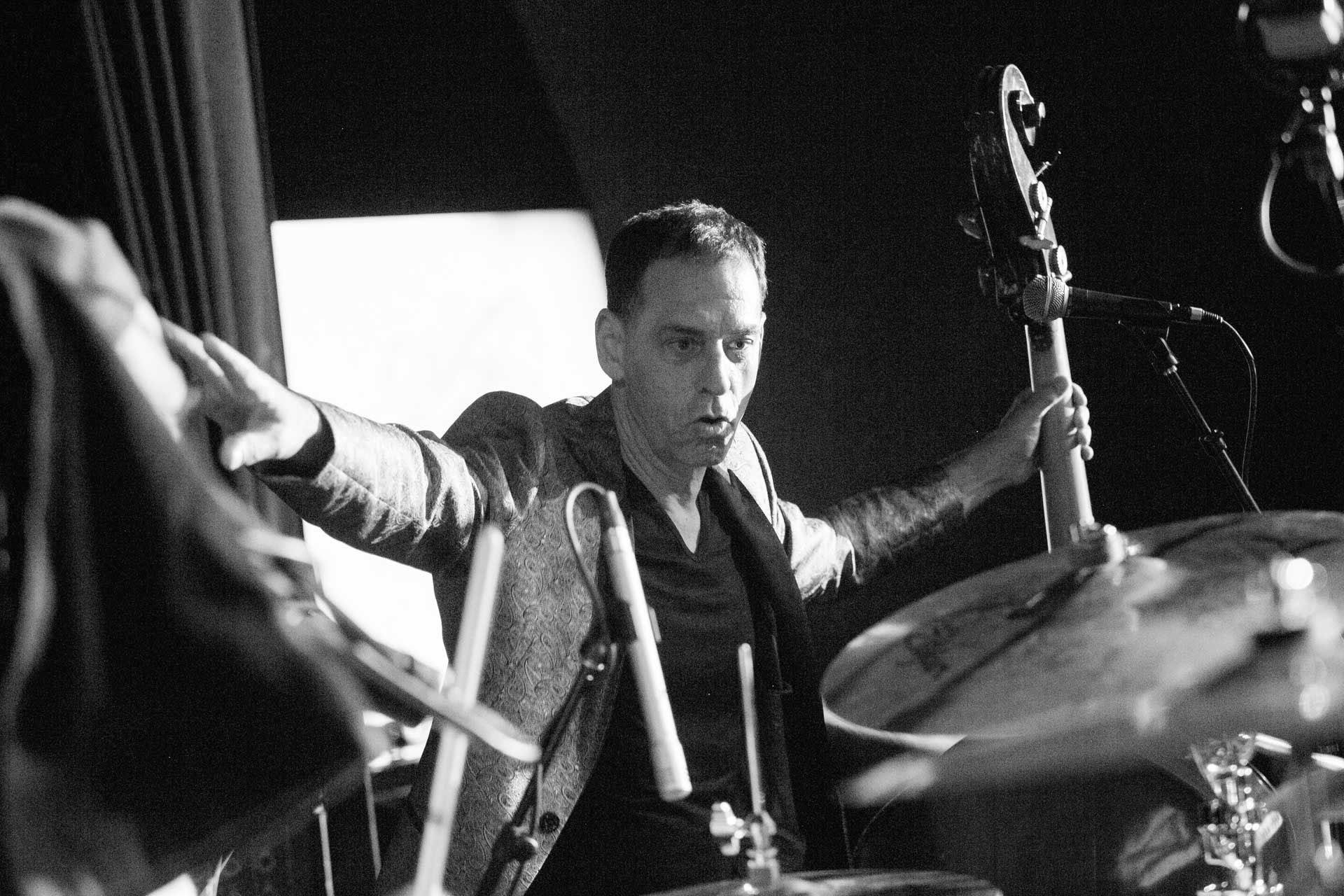 A man is playing drums in a black and white photo while holding a guitar.
