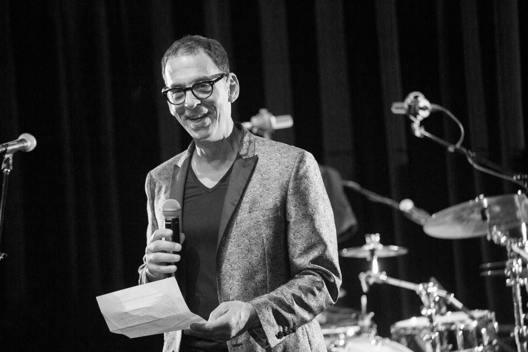 A man is holding a microphone and a piece of paper on a stage.