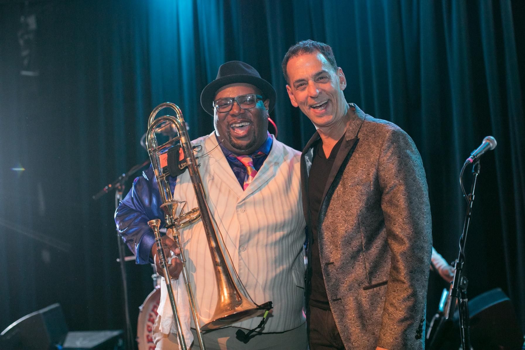 Two men are standing next to each other on a stage holding a trombone.