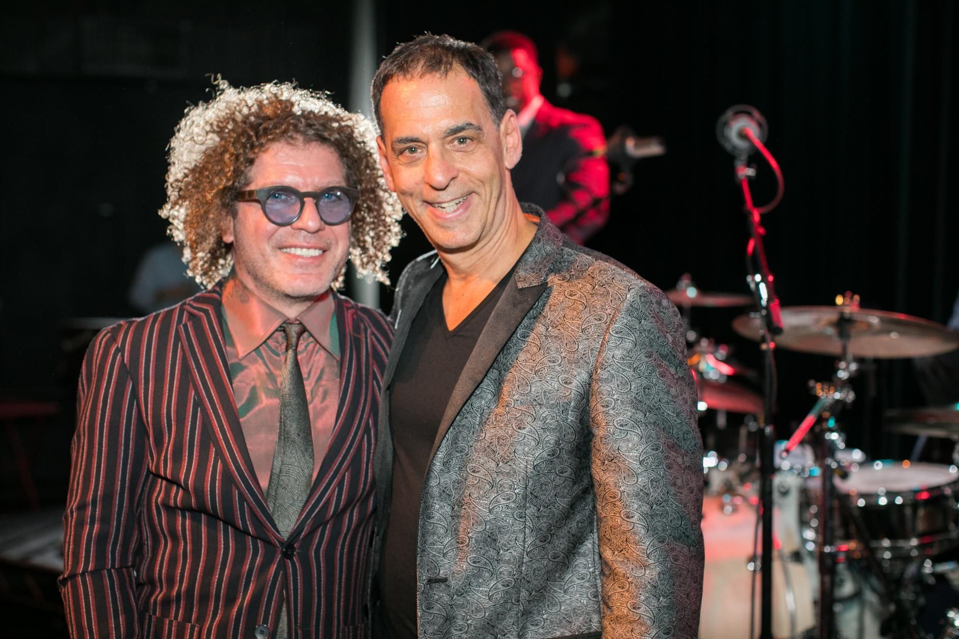 Two men are posing for a picture in front of a drum set.