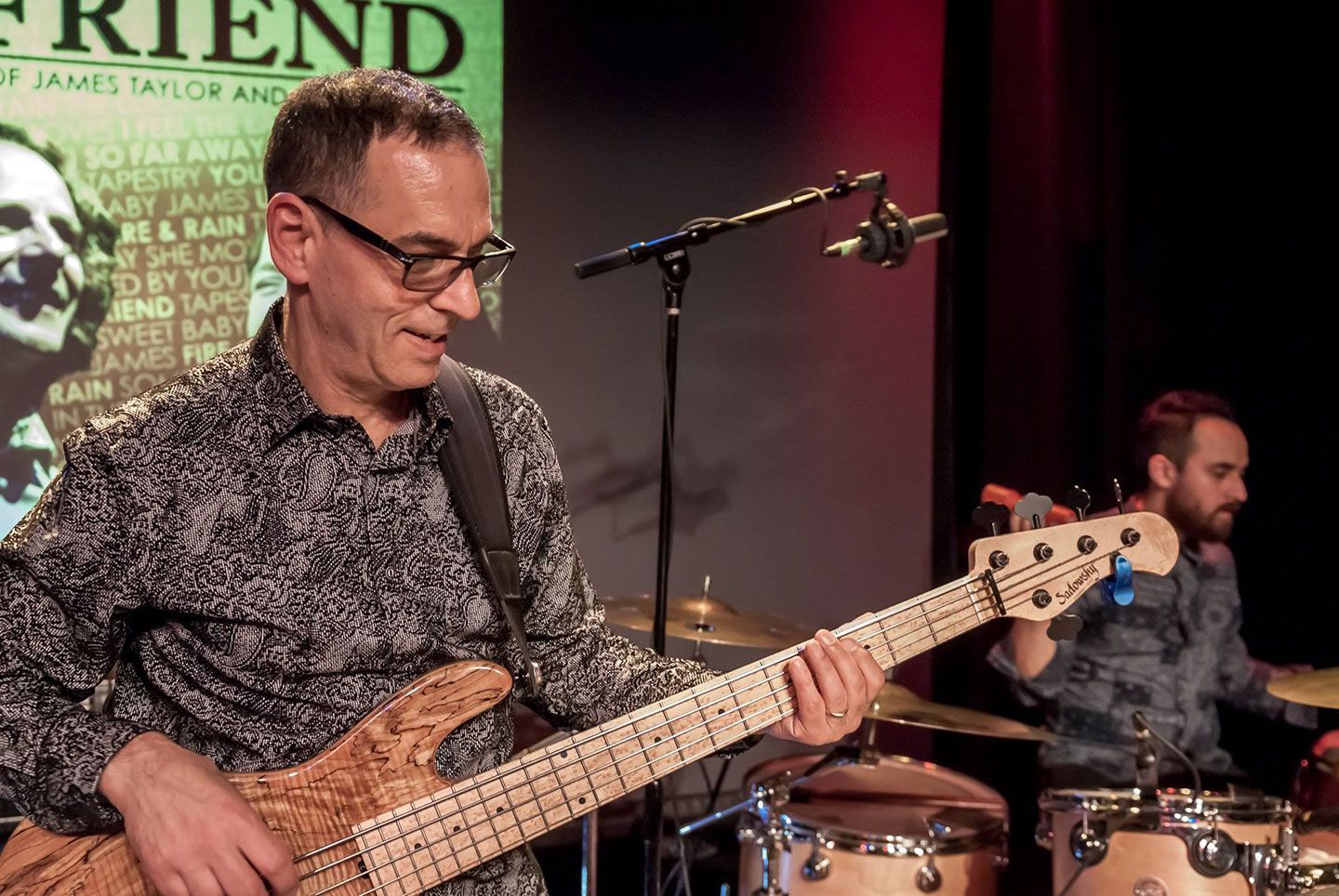 A man is playing a guitar in front of a sign that says friend