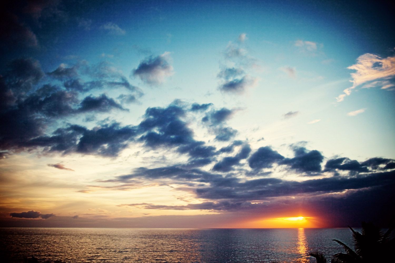 The sun is setting over the ocean with clouds in the sky.