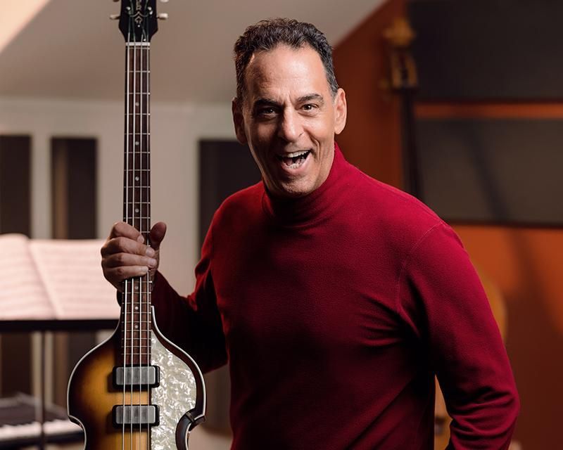 A man in a red turtleneck is holding a guitar