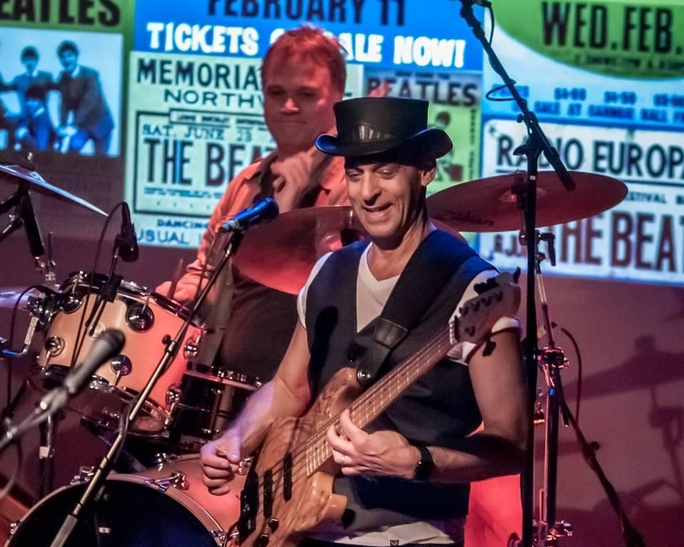 A man playing a guitar in front of a sign that says the beatles