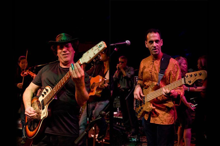 Two men are playing guitars on a stage in a dark room.