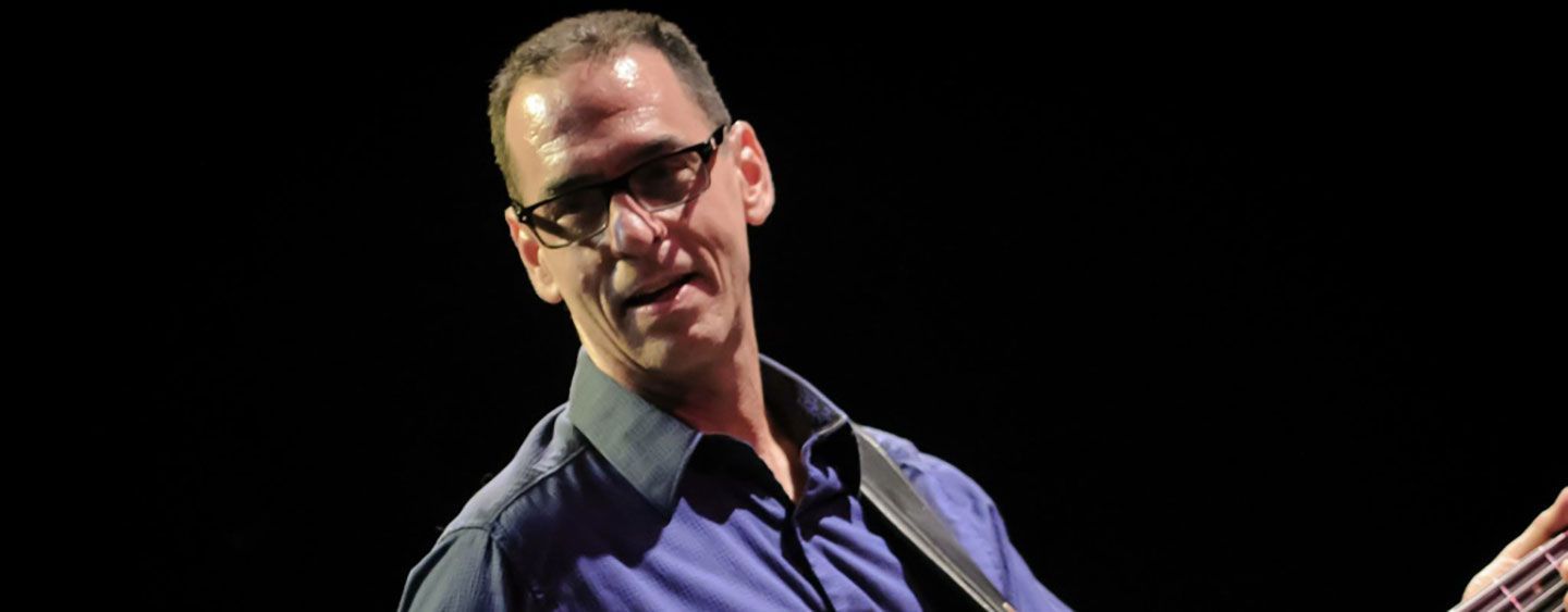 A man wearing glasses is playing a guitar in a dark room.