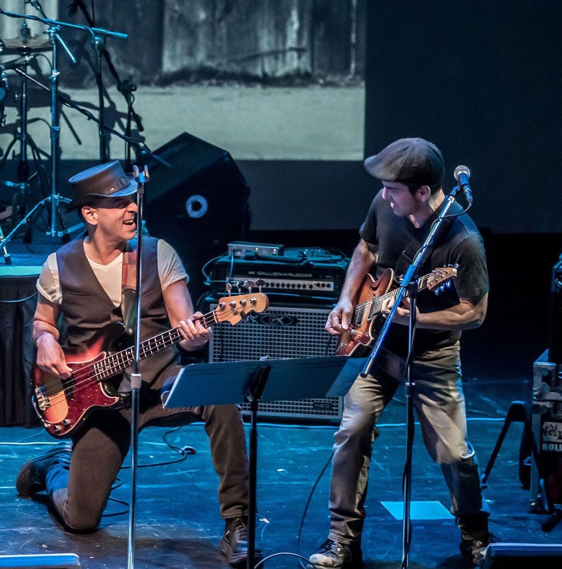 Two men on stage playing guitars and singing into microphones