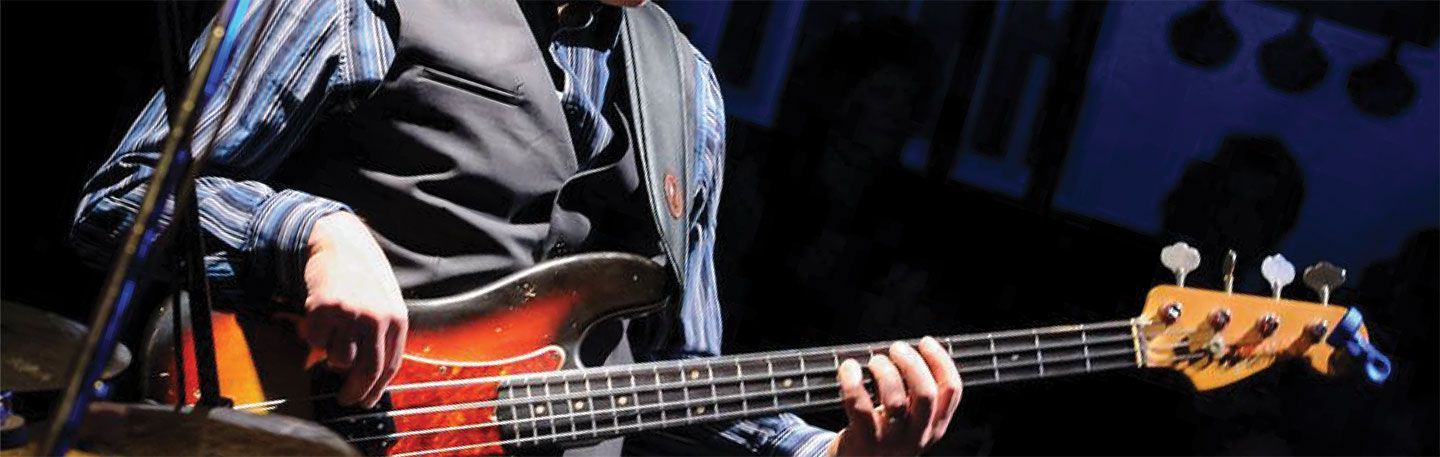 A man is playing a bass guitar on stage in front of a microphone.