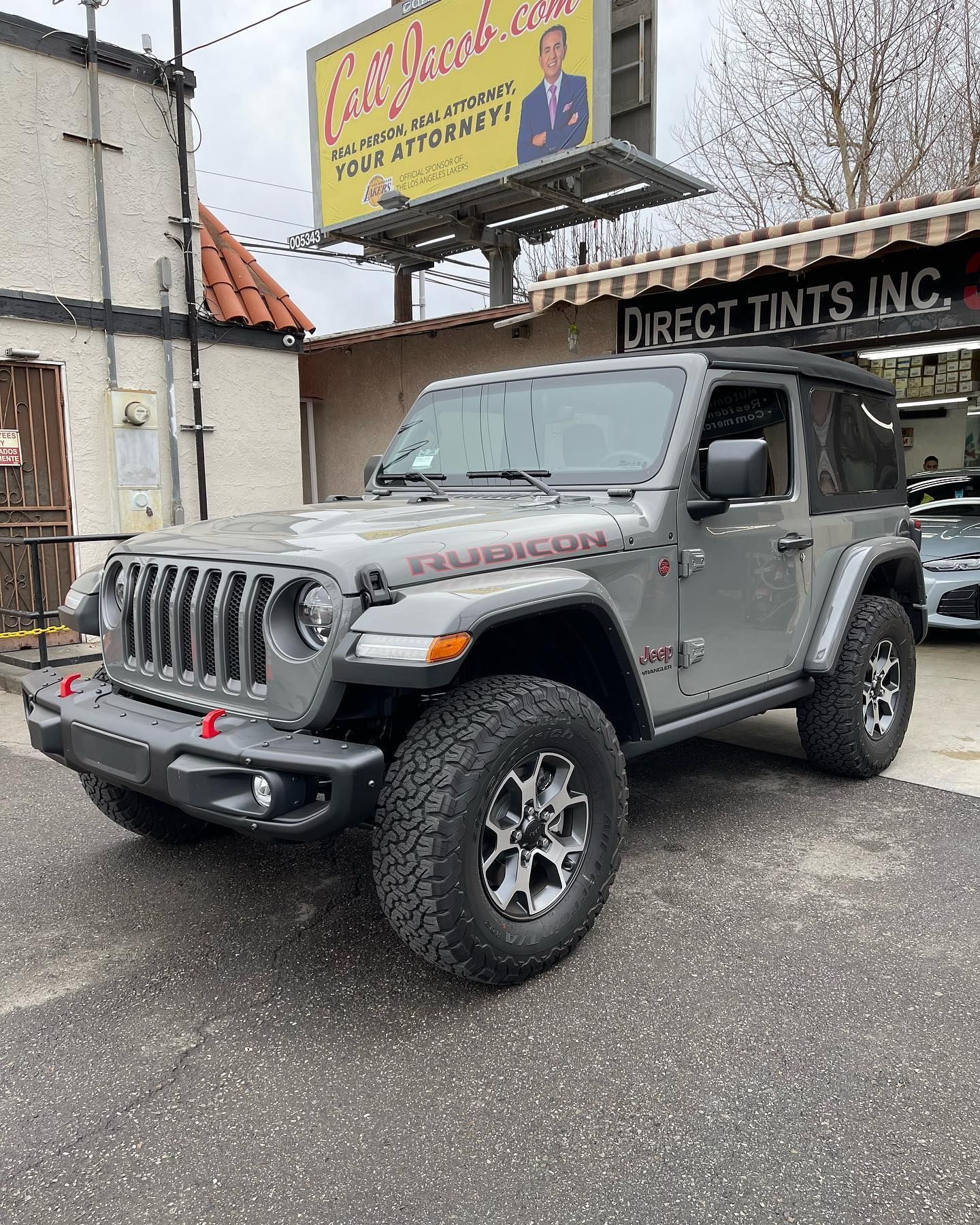 Gray Jeep Wrangler Rubicon parked in front of a storefront with a 