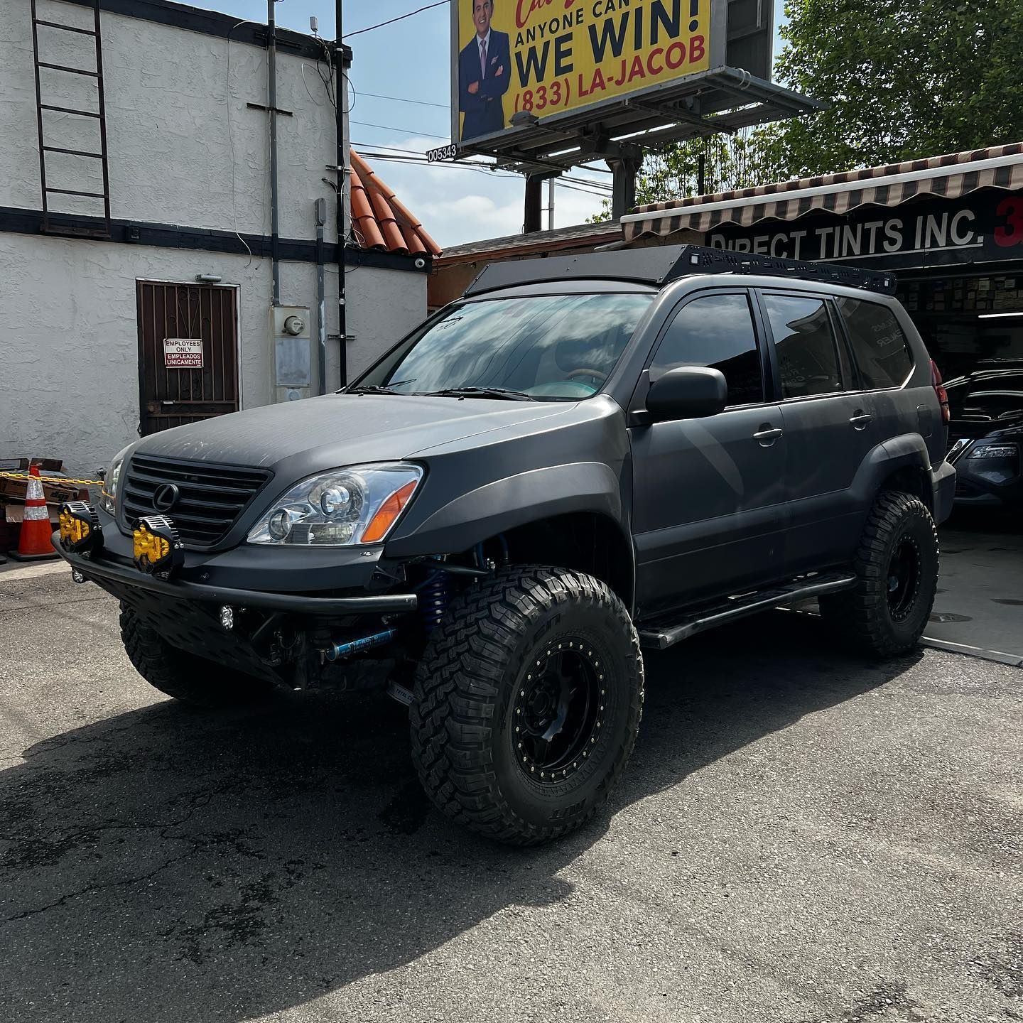 Dark gray lifted Lexus GX470 with large tires, parked in front of a tint shop.
