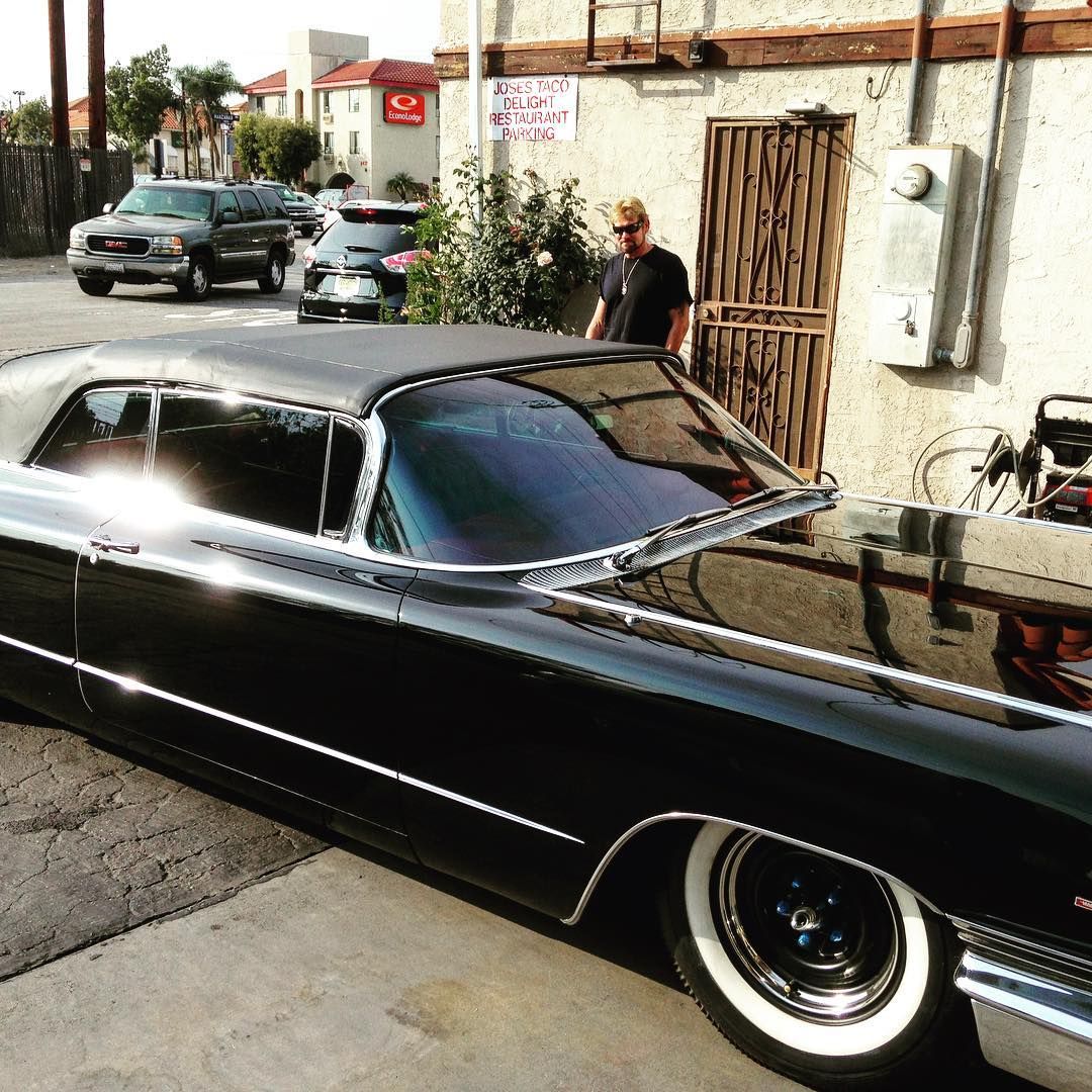 Black convertible car with white wall tires parked on the street; a man stands nearby.
