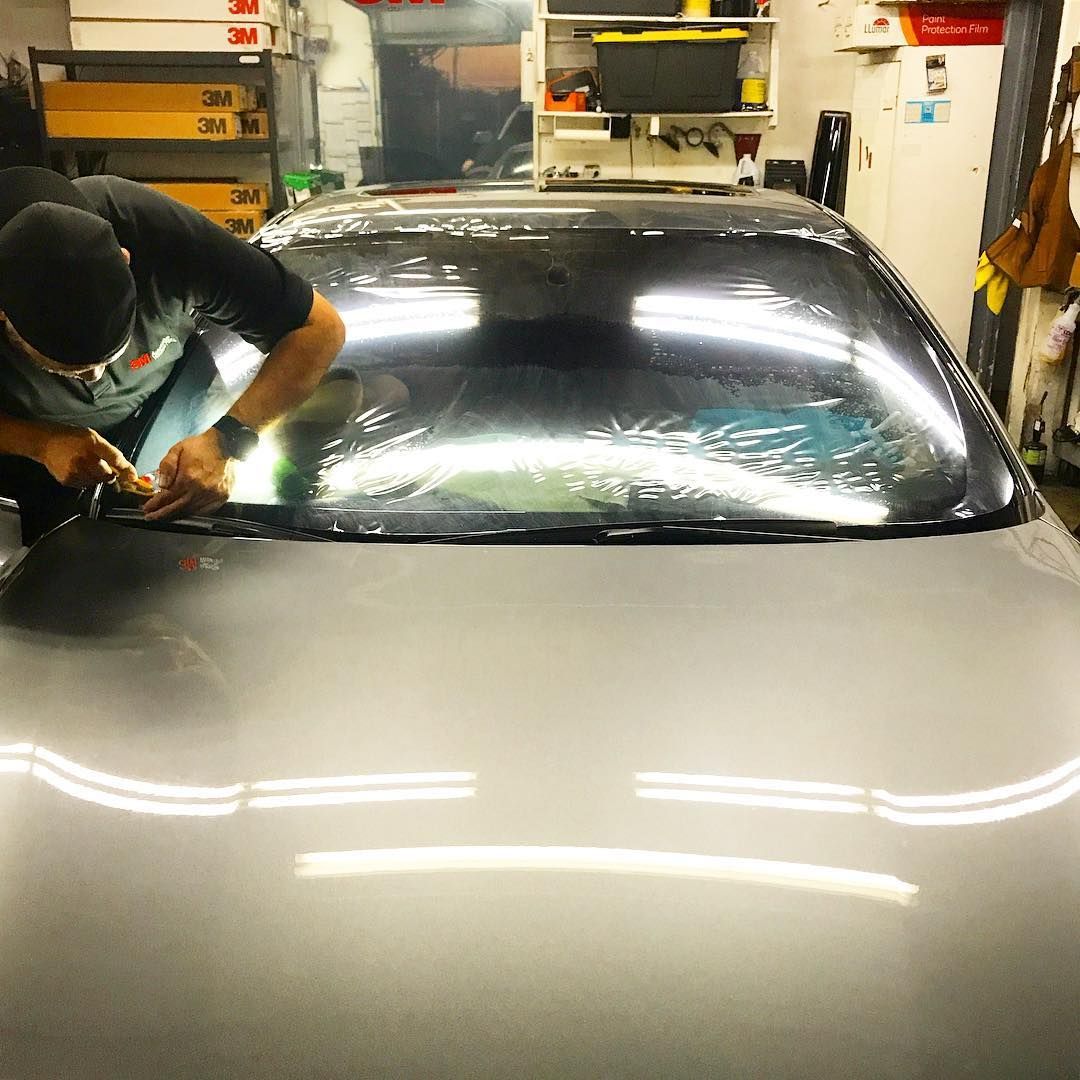 Person applying tint to a car window in a garage.