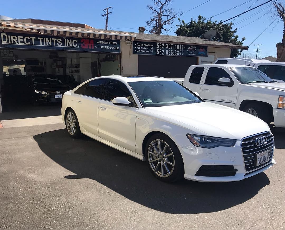 White Audi sedan with tinted windows parked in front of Direct Tints Inc. building on a sunny day.