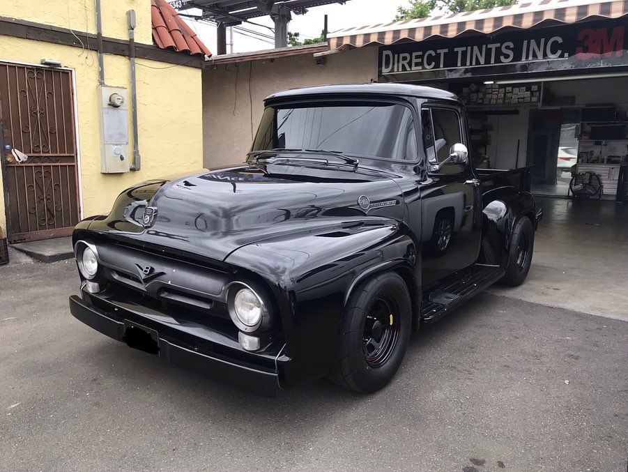 Black vintage Ford pickup truck parked in front of a shop.