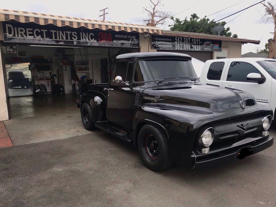 Black vintage Ford pickup truck parked outside a tint shop.