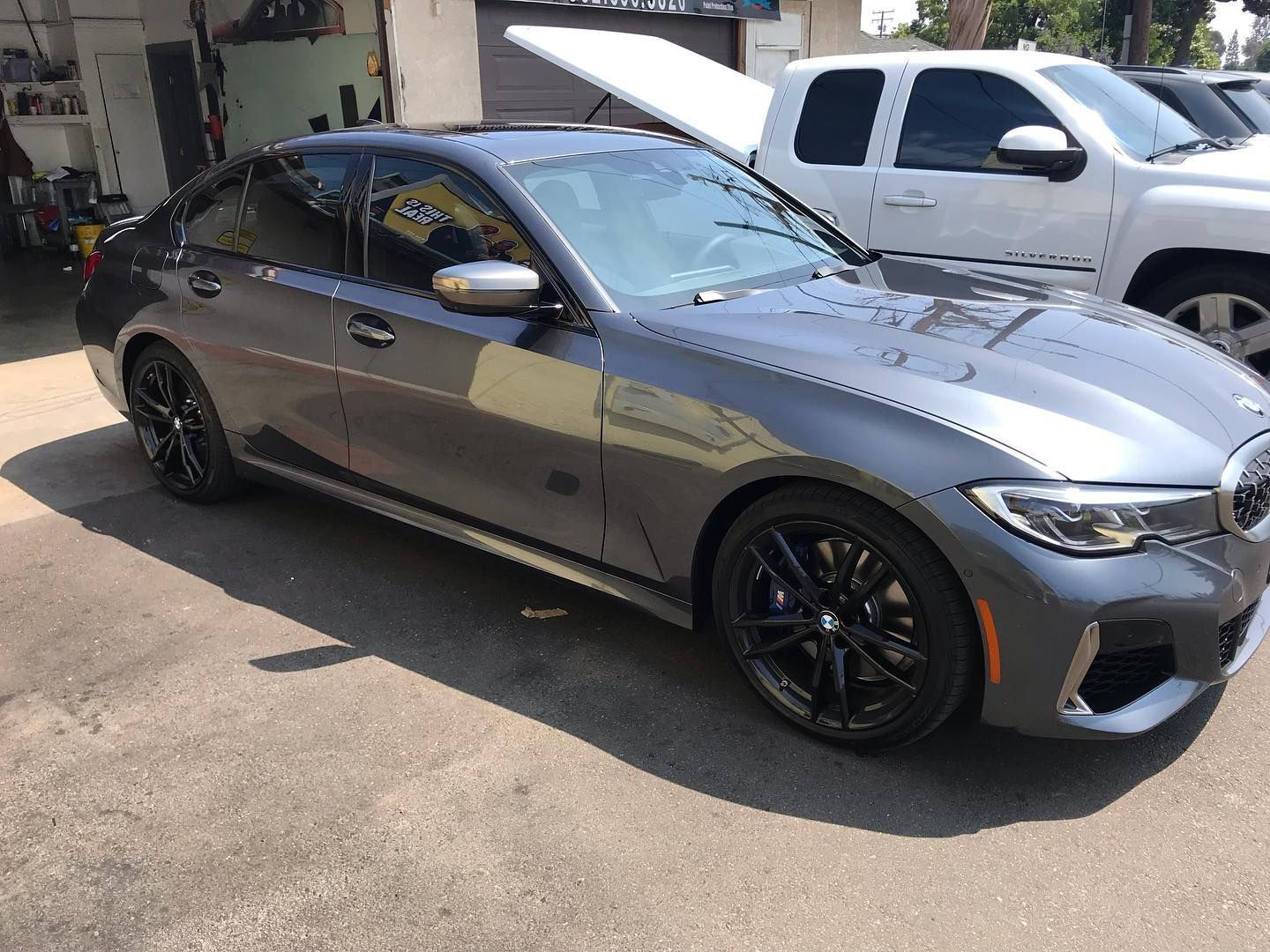 Gray BMW sedan parked on pavement next to white truck; sunny day.
