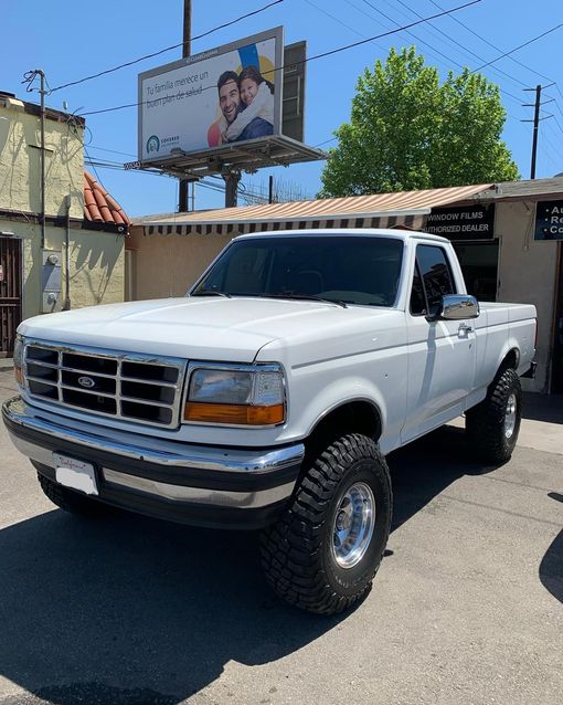 White Ford pickup truck with large tires parked in front of a building.