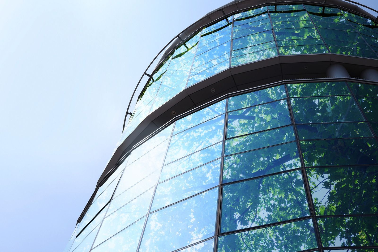 Glass-paneled building reflects blue sky and green trees.