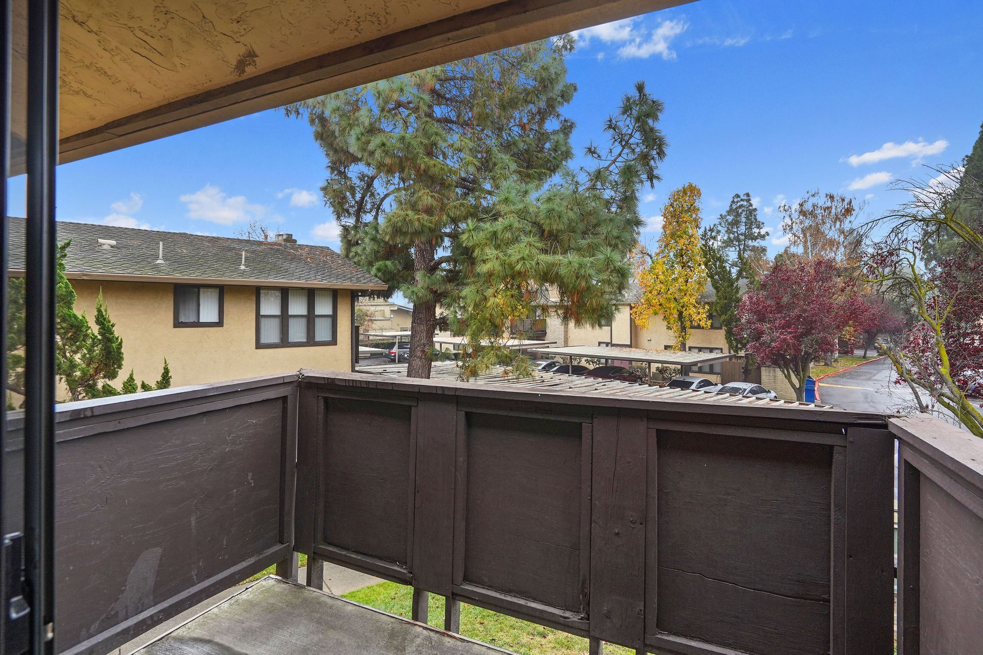 Balcony overlooking a courtyard with trees and nearby apartment buildings on a sunny day