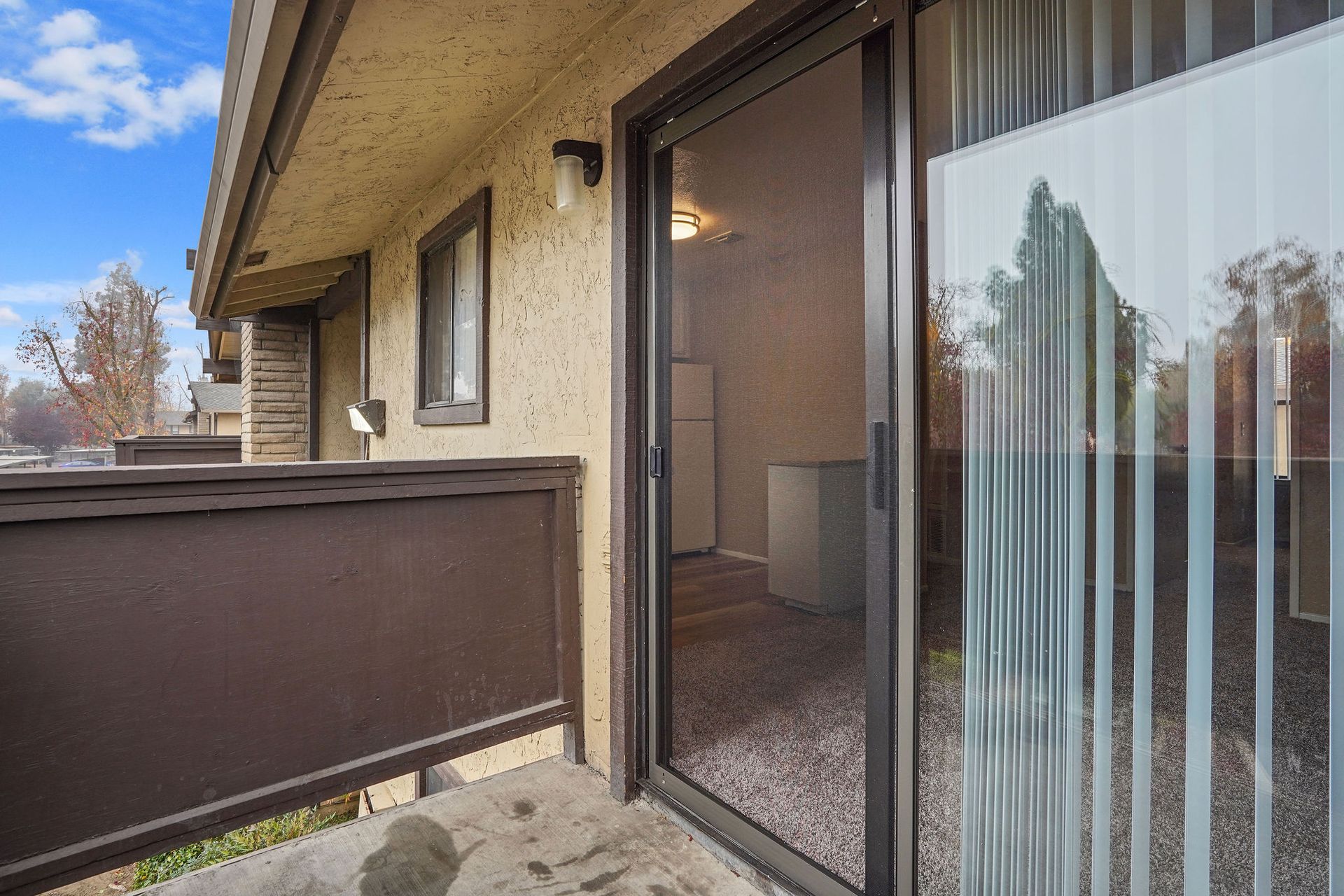 Apartment balcony with brown railing and sliding glass door, overlooking trees on a cloudy day