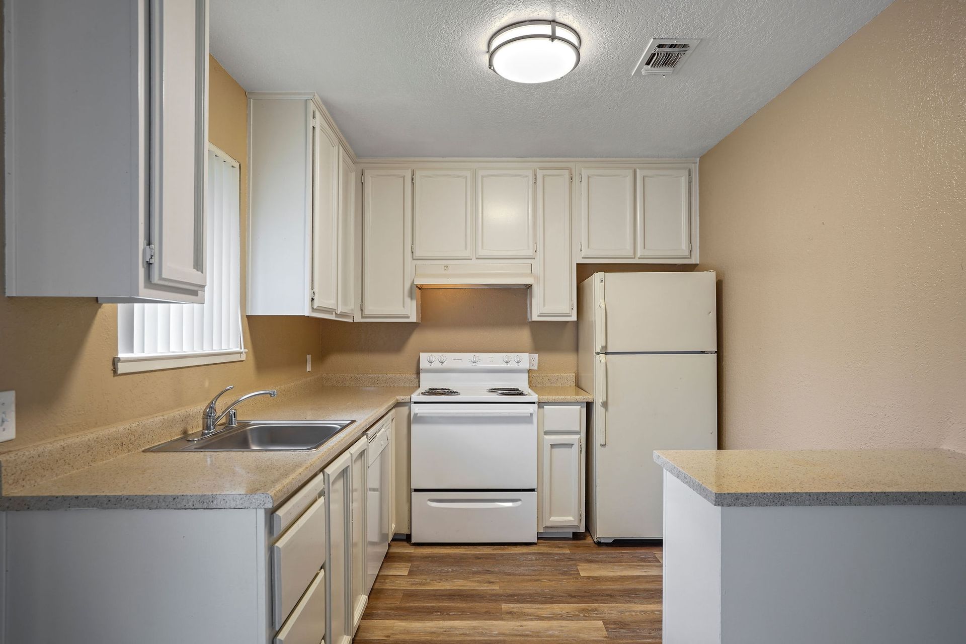 Small white kitchen with cabinets, sink, stove, refrigerator, and beige walls.