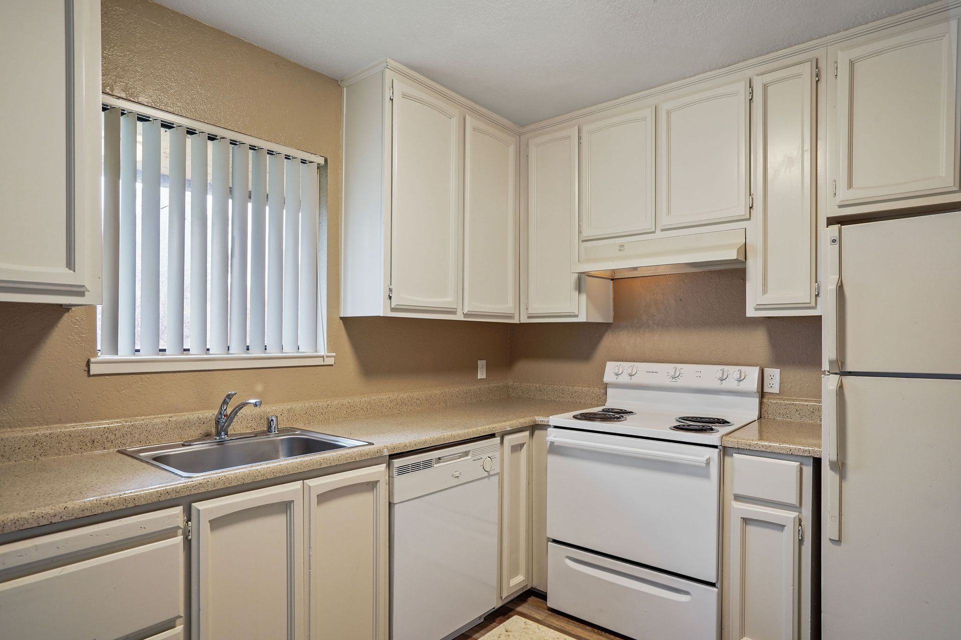 White kitchen with beige countertops, sink by window, and white stove and cabinets