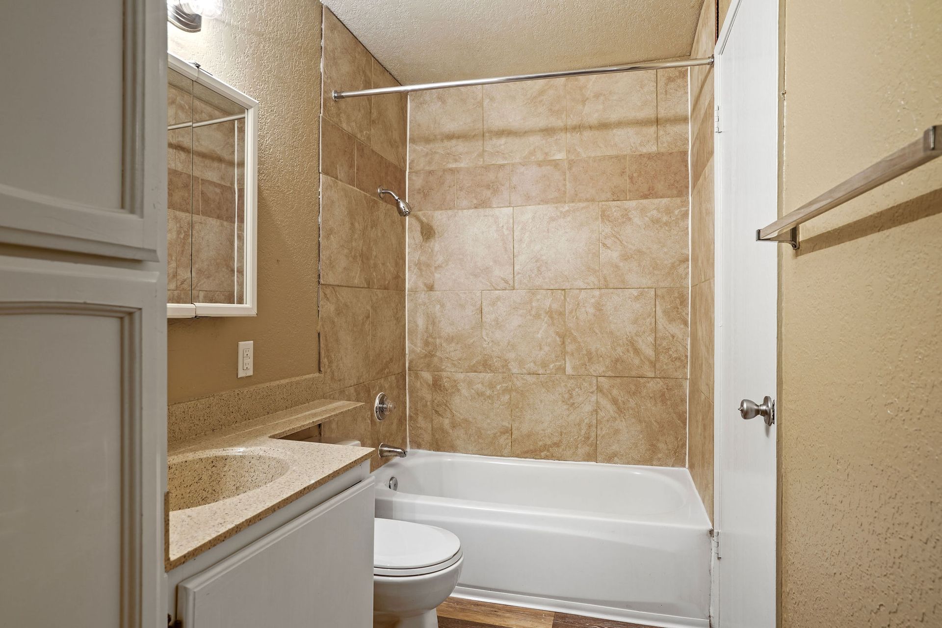 Small beige tiled bathroom with a tub, toilet, sink, mirror, and towel bar.