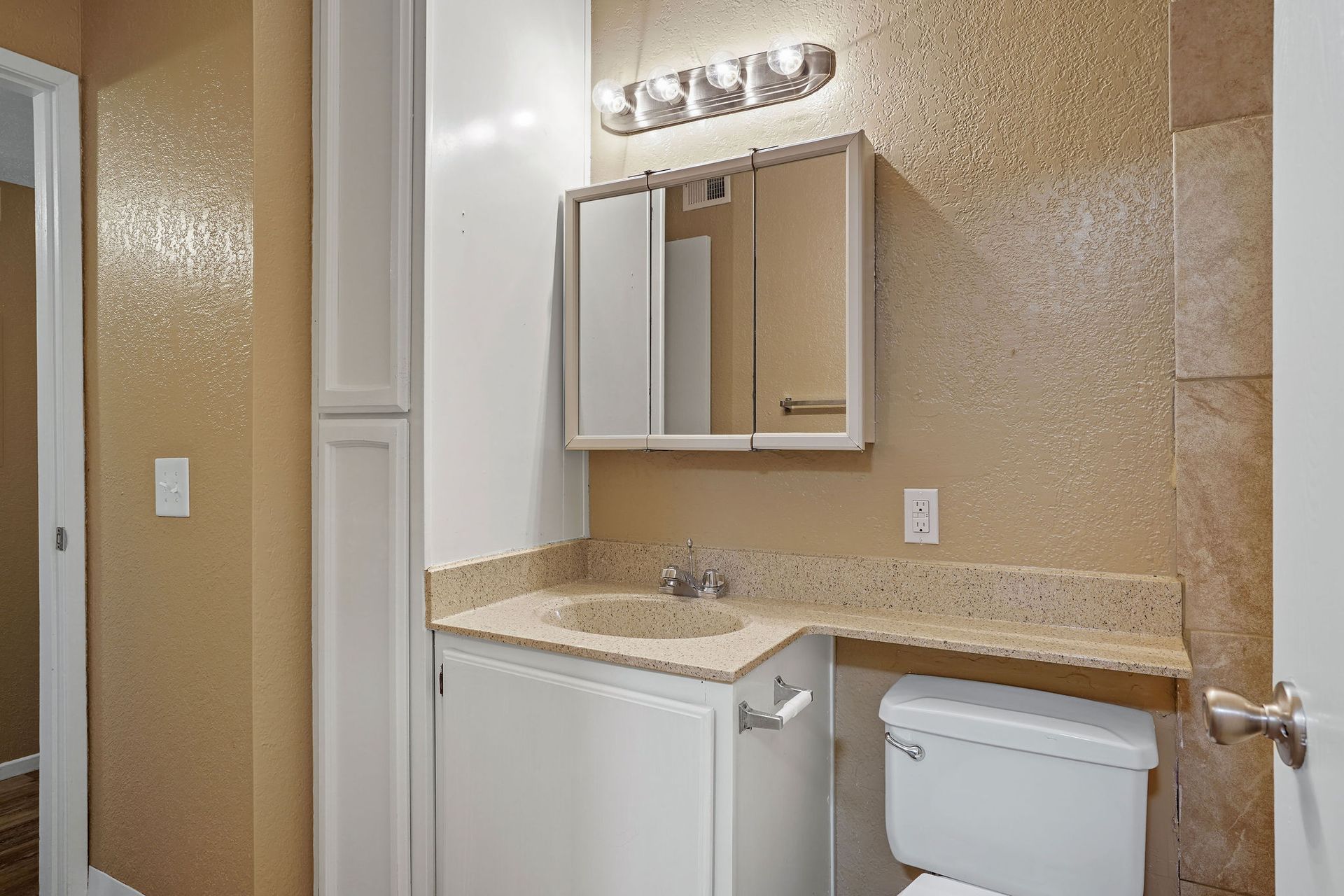 Small bathroom with beige walls, vanity, mirror cabinet, and toilet under vanity lights