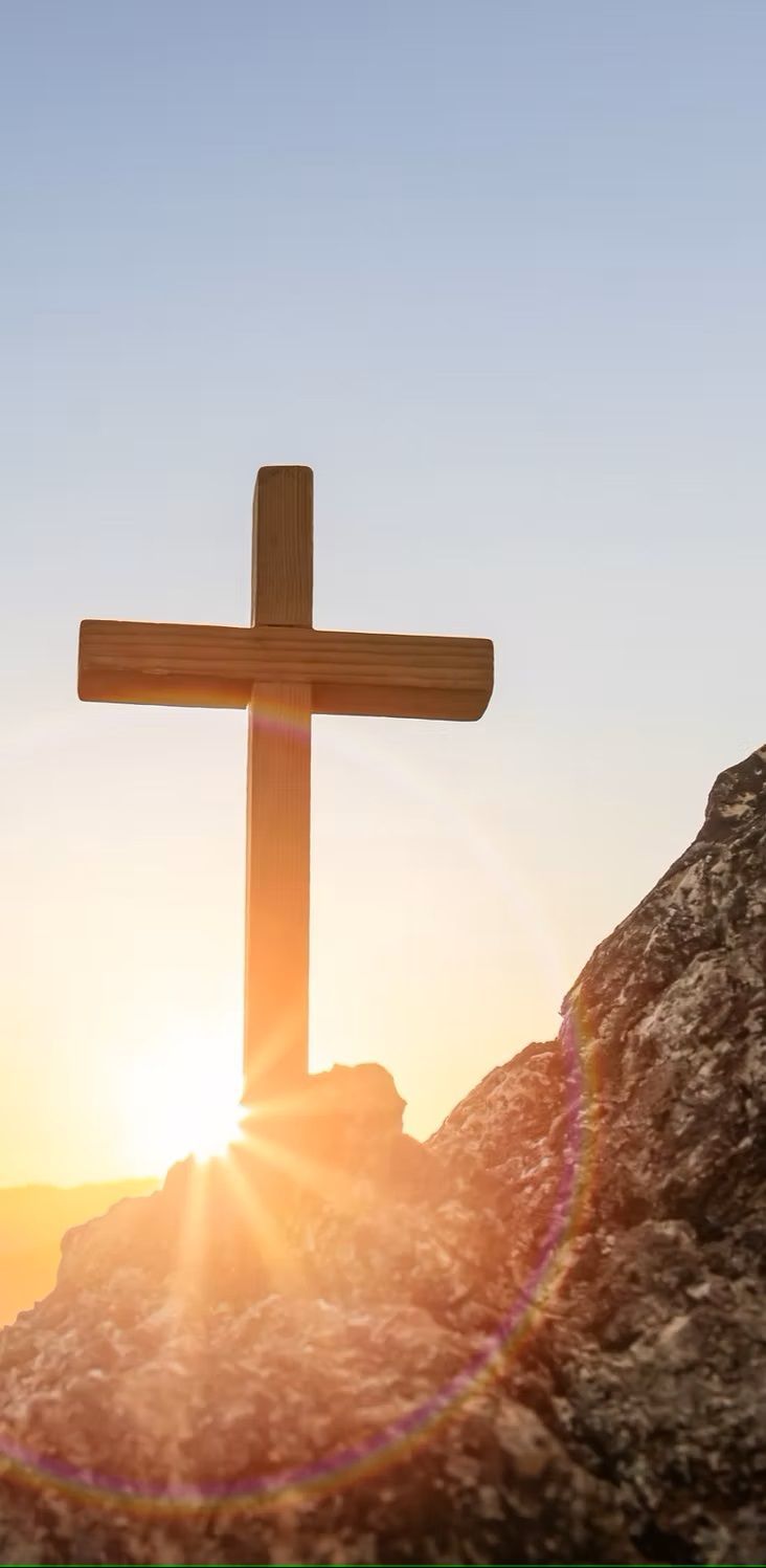 A wooden cross is sitting on top of a rock at sunset.