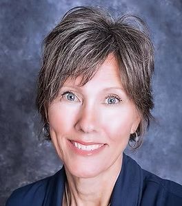 A woman wearing a blue jacket and earrings is smiling for the camera.