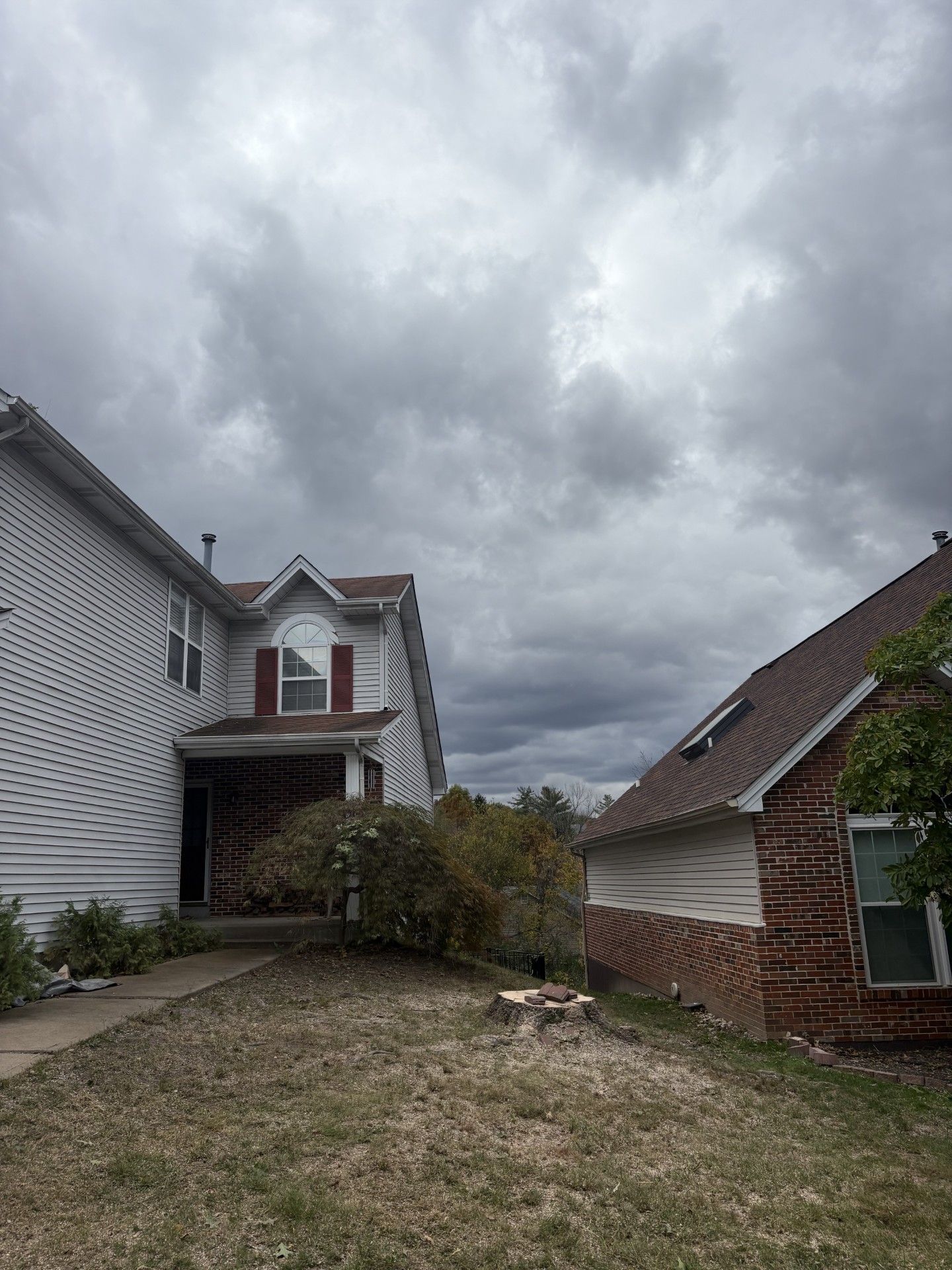 Two-story houses under a cloudy sky. One has white siding, a red roof, and a small front porch. The other is red brick.