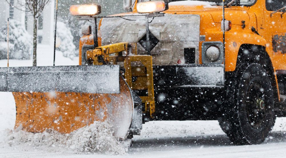Un chasse-neige déneige dans une rue enneigée.