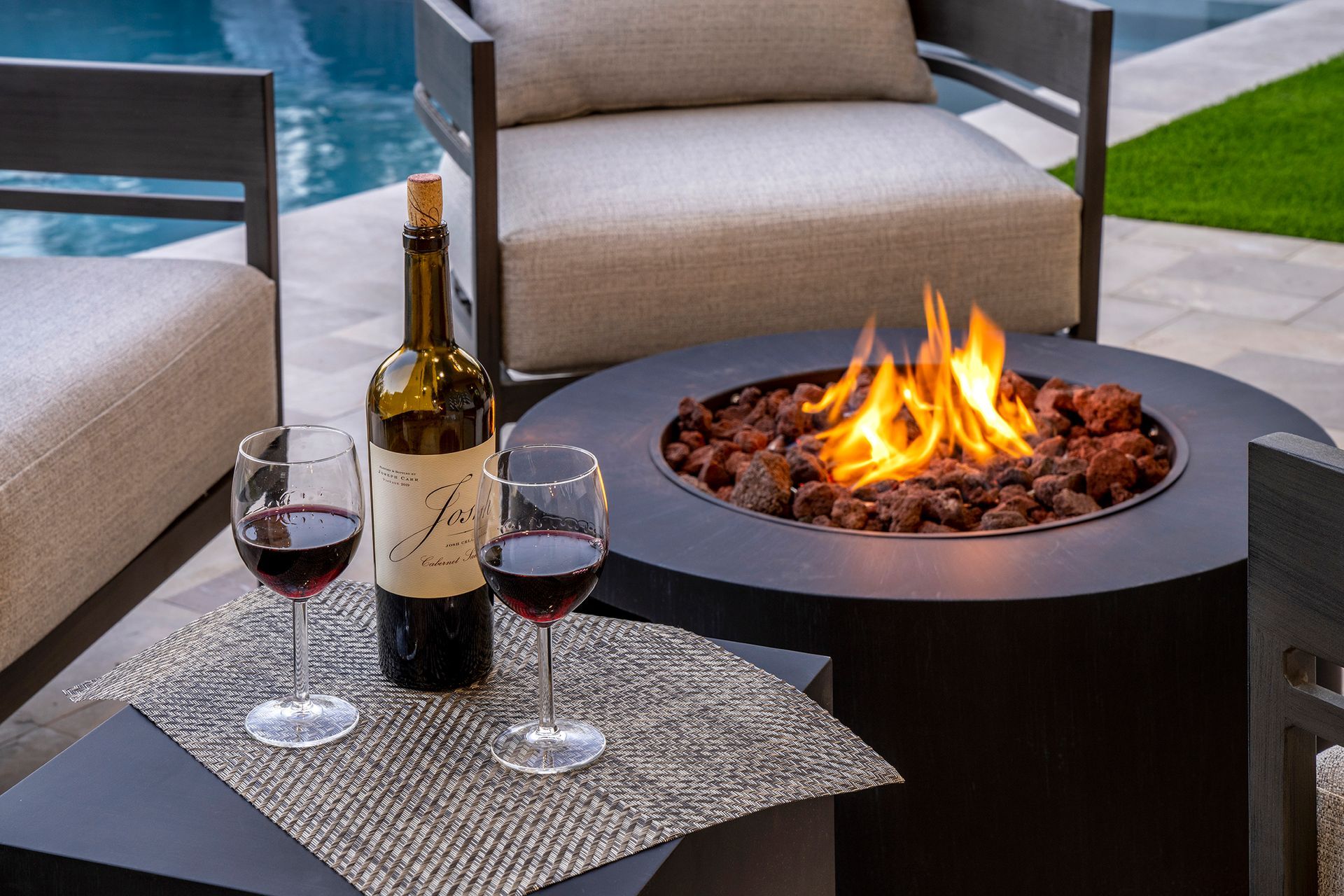 a bottle of wine and two glasses of wine are on a table next to a fire pit .