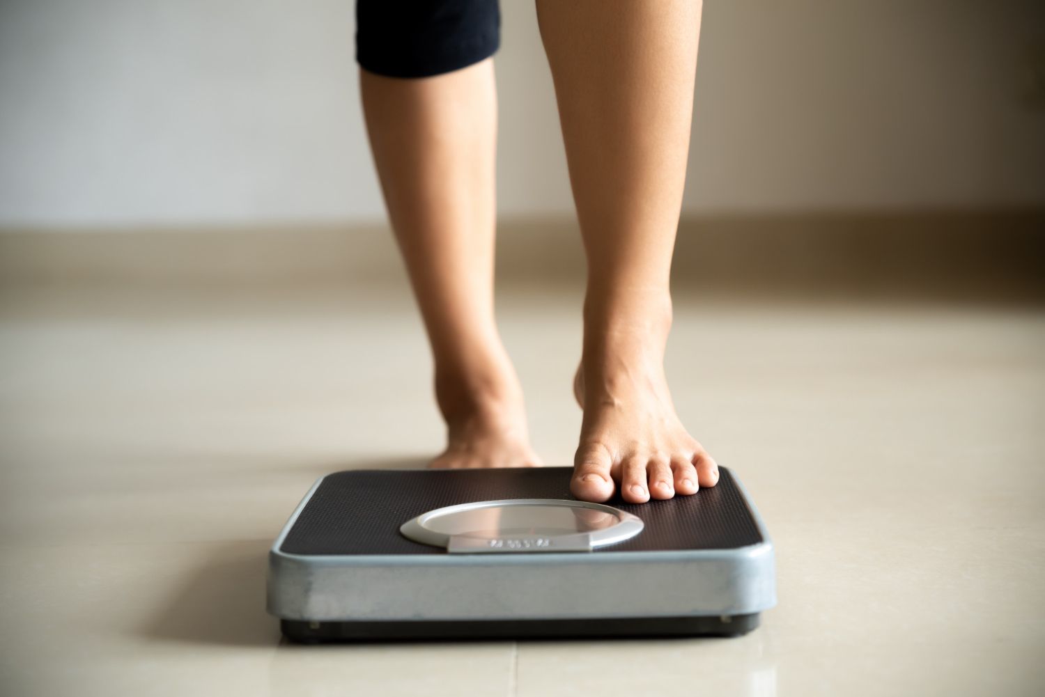 Person's bare feet standing on a black and silver scale, indoors.