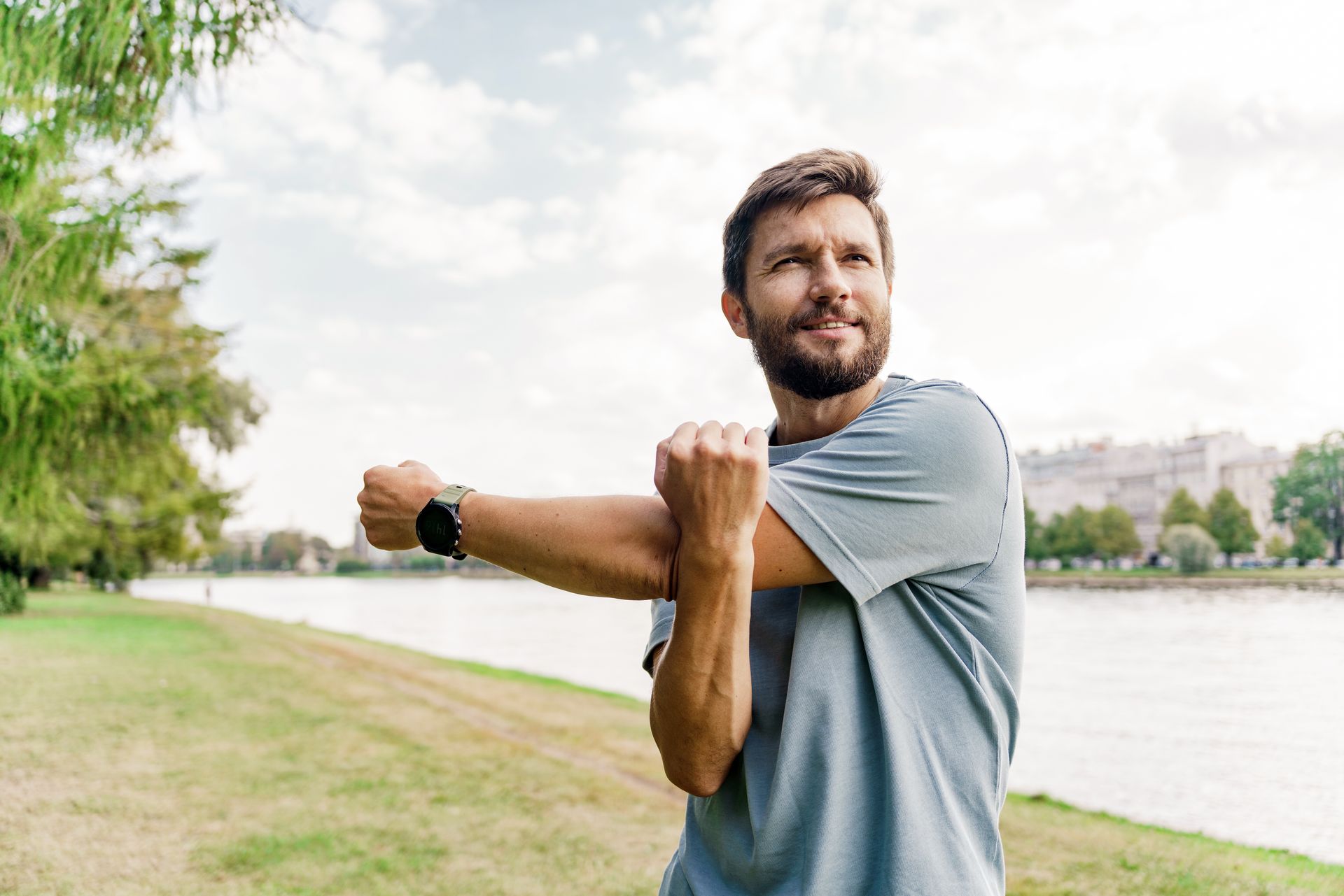 A man is stretching his arms in a park near a lake.