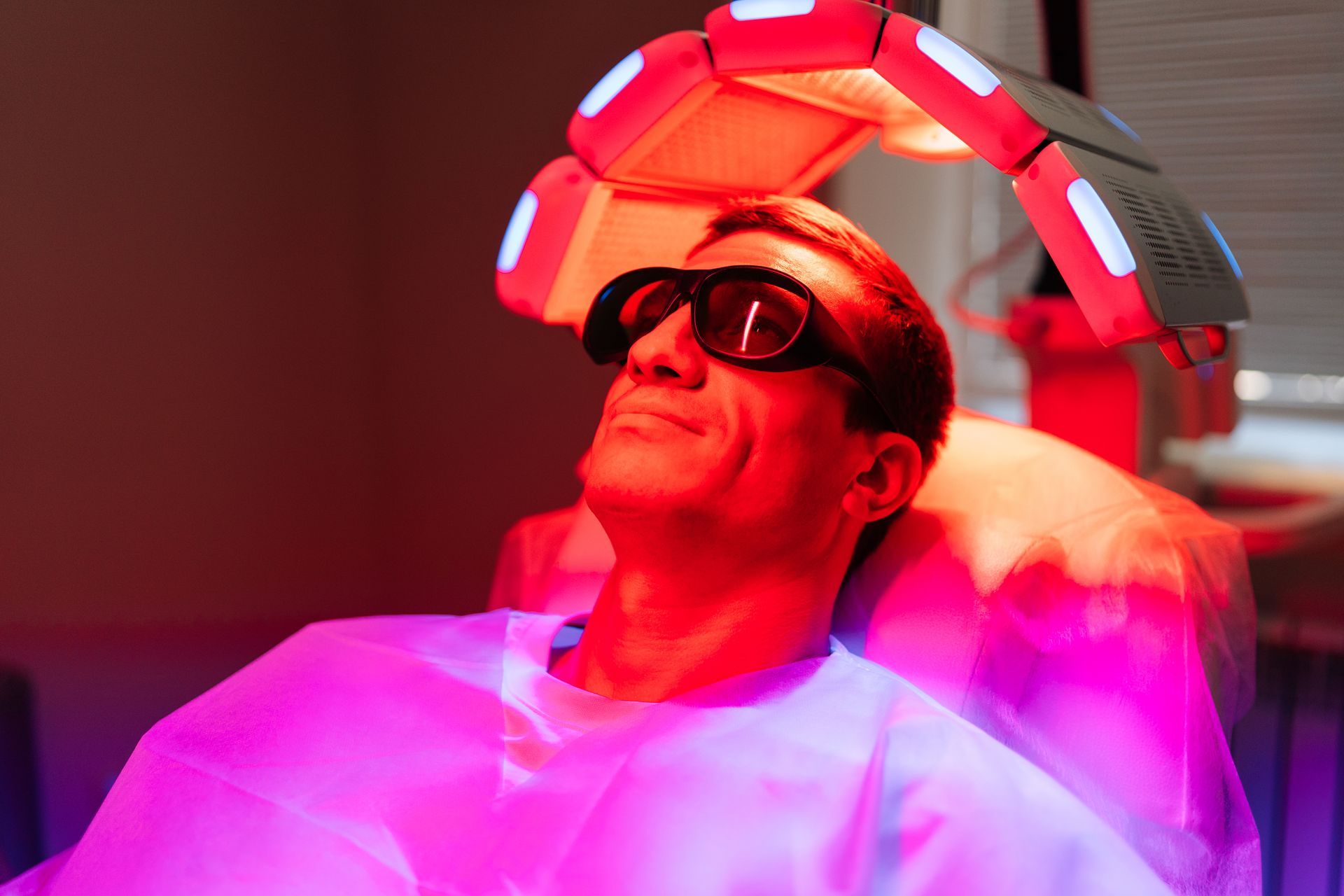 Man wearing glasses under red LED light therapy machine.