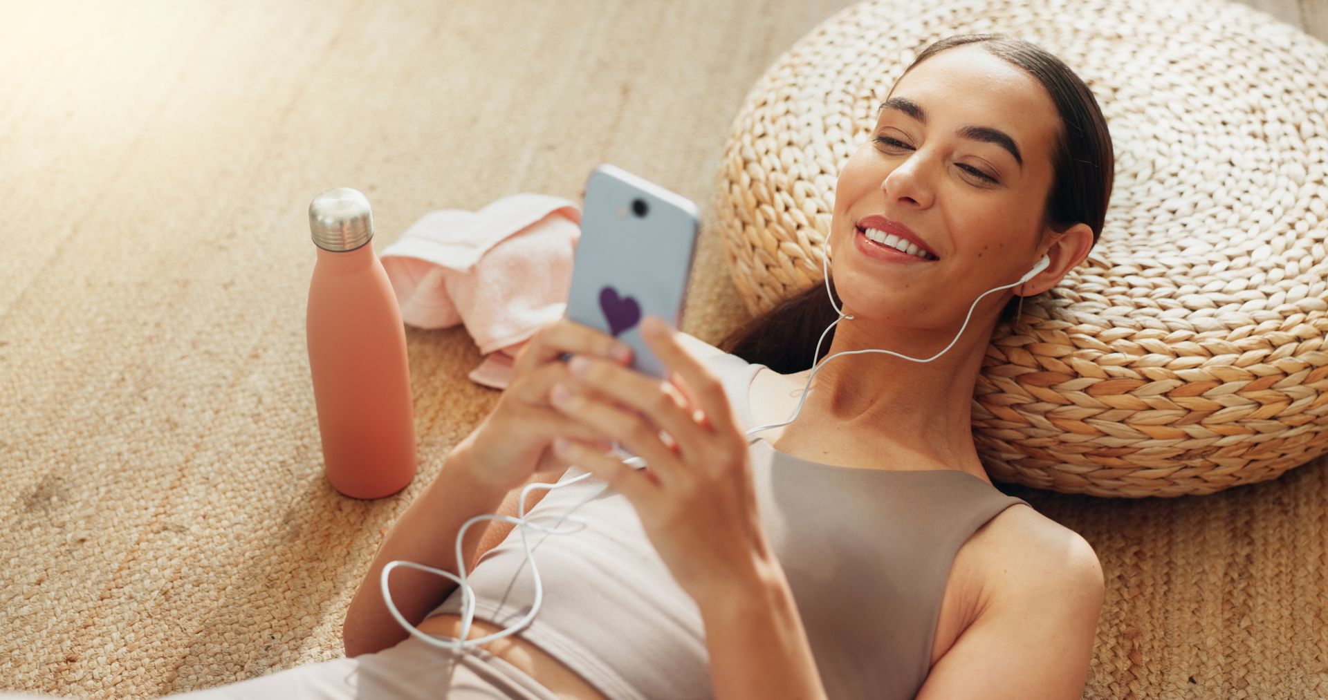 A woman is sitting on the floor listening to music on her phone.