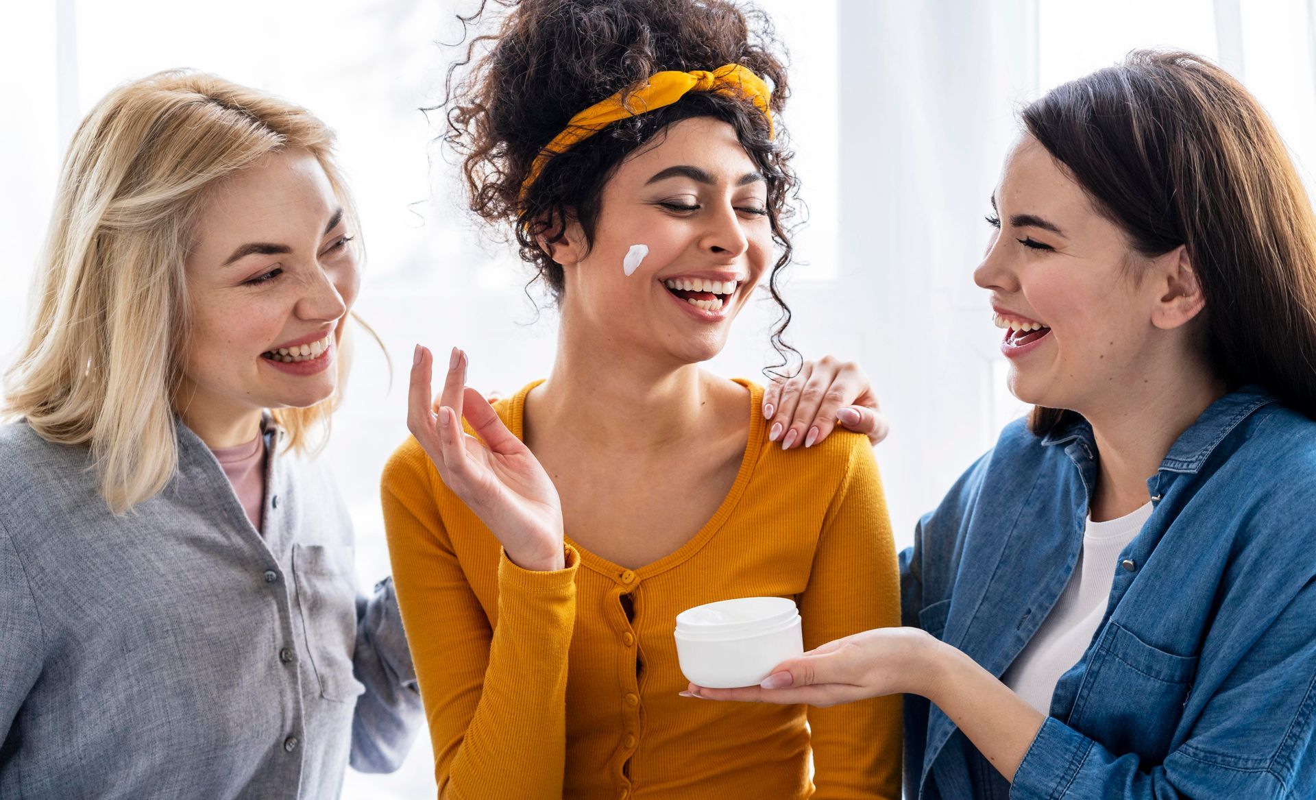 Three women are laughing and applying cream to each other 's faces.