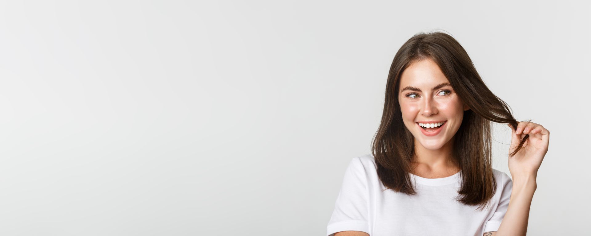 A woman in a white t-shirt is smiling and holding her hair.