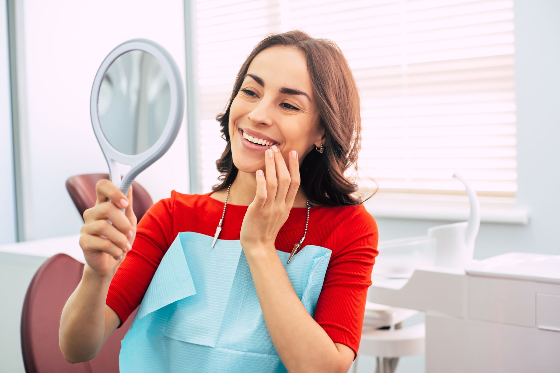 A woman is looking at her teeth in a mirror at the dentist.