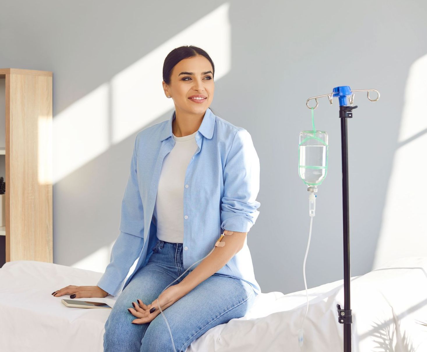 A woman is sitting on a bed with an iv in her arm.