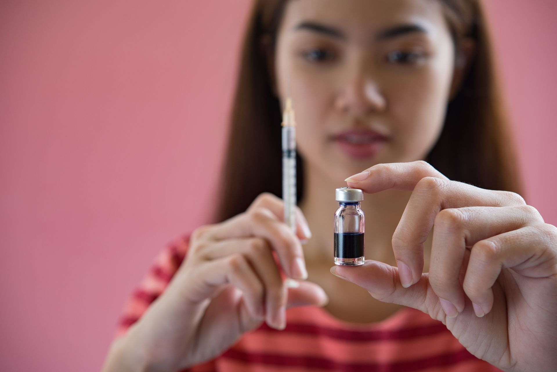 A woman is holding a bottle of vaccine and a syringe.