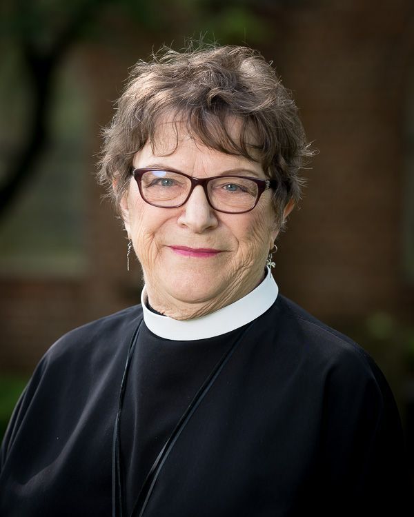 A woman wearing glasses and a black robe is smiling for the camera.