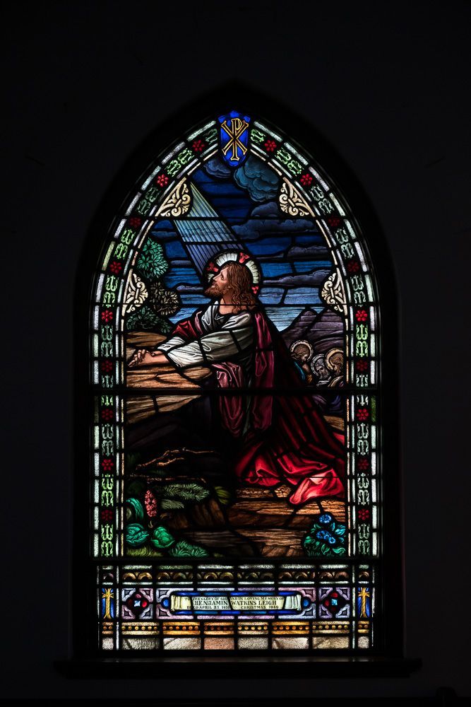 A stained glass window in a church depicting jesus praying in the garden.